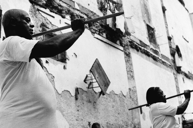 Black and white image of a group of people exercising with wooden poles. 